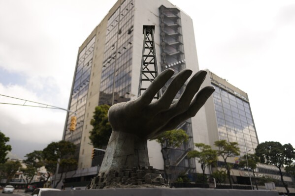 FILE - A sculpture of a hand holding an oil well stands by the state-run oil company Petroleos de Venezuela S.A. (PDVSA), behind, in Caracas, Venezuela, Tuesday, March 21 2023. (AP Photo/Ariana Cubillos, File)