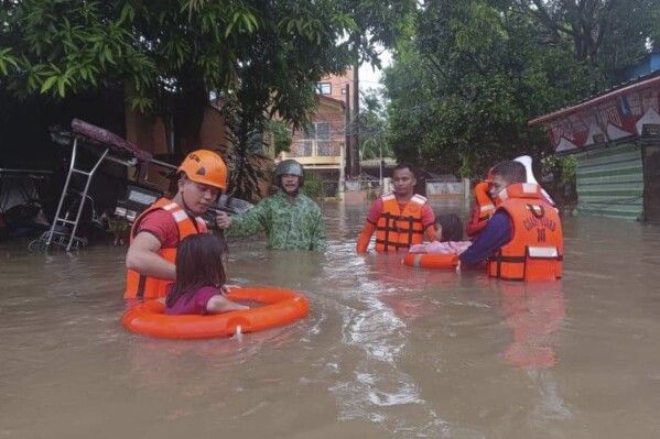 In this handout photo provided by the Philippine Coast Guard, members of the Coast Guard Station Southern Quezon rescue residents from their flooded homes in Lucena, Quezon province, Philippines on Sunday, May 26, 2024. Typhoon Ewiniar, locally known as Aghon, on Tuesday hit the Philippines, blowing away people and leaving at least seven dead, mostly due to floods or toppled trees. Several seaports have been shut down, stranding thousands of passengers, officials said. (Philippine Coast Guard via AP)