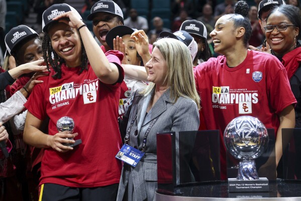 FILE - Southern California's McKenzie Forbes reacts after being presented the Pac-12 tournament Most Valuable Player trophy by Pac-12 Commissioner Teresa Gould after USC defeated Stanford in an NCAA college basketball game for the championship of the Pac-12 tournament March 10, 2024, in Las Vegas. The NCAA and the nation's five biggest conferences have agreed to pay nearly $2.8 billion to settle a host of antitrust claims,a monumental decision that sets the stage for a groundbreaking revenue-sharing model that could start directing millions of dollars directly to athletes as soon as the 2025 fall semester. (AP Photo/Ian Maule, File)