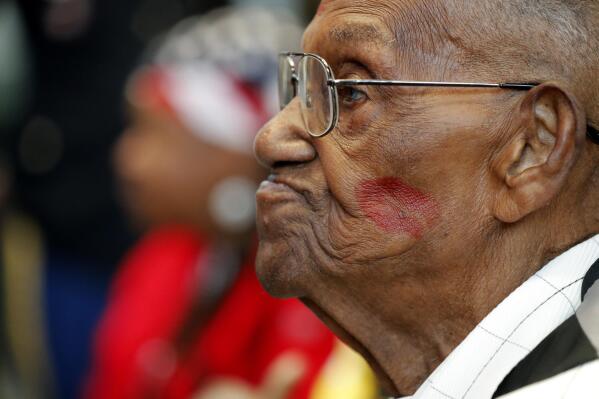 FILE - In this Sept. 12, 2019 file photo, World War II veteran Lawrence Brooks sports a lipstick kiss on his cheek, planted by a member of the singing group Victory Belles, as he celebrates his 110th birthday at the National World War II Museum in New Orleans.  (AP Photo/Gerald Herbert, File)