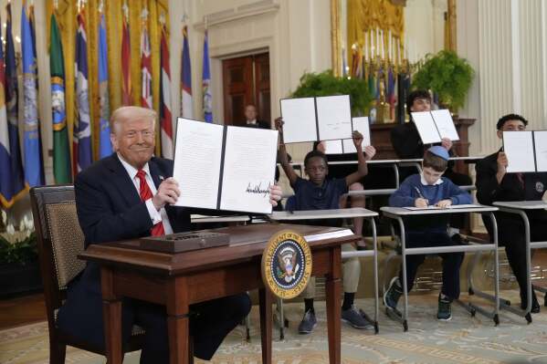 U.S. President Donald Trump holds up a signed executive order as youths hold up copies of the executive order they signed at an education event in the East Room of the White House in Washington, March 20, 2025. (AP Photo/Ben Curtis)