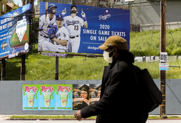 A pedestrian wears a hat and a face mask on Sunset Blvd., in the Echo Park neighborhood of Los Angeles, Thursday, April 2, 2020. Major League Baseball opening day was to have been Thursday, March 26, but was pushed back to mid-May at the earliest because of the coronavirus outbreak. The spring training schedule was cut short on March 12 because on the pandemic, and it remains unclear when and if baseball can resume. (AP Photo/Damian Dovarganes)
