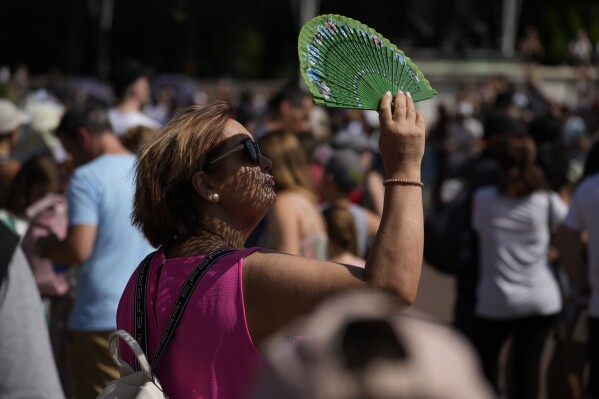 FILE - A tourist uses a fan to shade her face from the sun while waiting to watch the Changing of the Guard ceremony outside Buckingham Palace, during hot weather in London, July 18, 2022. Crushing temperatures that blanketed Europe during the summer of 2022 may have led to more than 61,000 heat-related deaths, according to a study published Monday, July 10, 2023. (AP Photo/Matt Dunham, File)