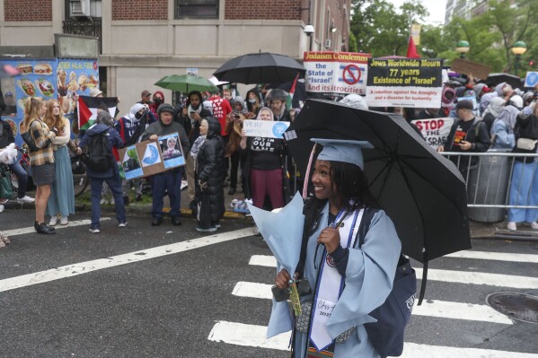 Alumni will take photos in New York on Wednesday, May 21, 2025 in front of a group of people protesting to support Palestinians across the street from the main gate of Columbia University. (AP Photo/Heather Khalifa)