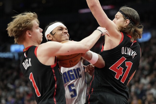 Orlando Magic forward Paolo Banchero (5) tries to drive between Toronto Raptors' Gradey Dick (1) and Kelly Olynyk (41) during the second half of an NBA basketball game Friday, March 15, 2024, in Toronto. (Frank Gunn/The Canadian Press via AP)