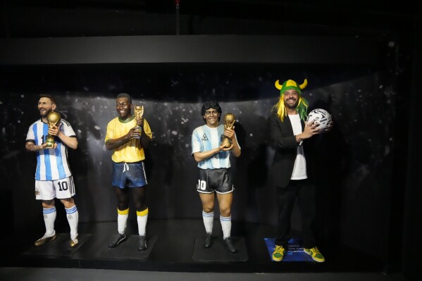 A Brazil soccer fan poses next to life-size statues of South American soccer stars, from left, Lionel Messi, Pele and Diego Maradona at the CONMEBOL museum on the day of its re-inauguration in Luque, Paraguay, Monday, March 18, 2024. (AP Photo/Jorge Saenz)