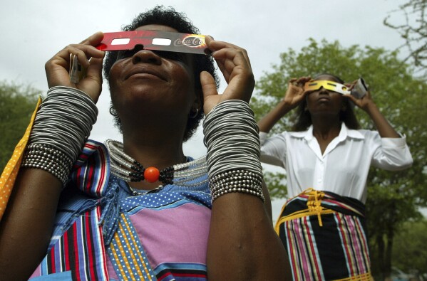 FILE - Lucy Maphiri, left, and Margaret Makuya watch the total solar eclipse over Shingwedzi camp in the Kruger National Park, South Africa, Wednesday, Dec. 4, 2002. (AP Photo/Jon Hrusa, File)