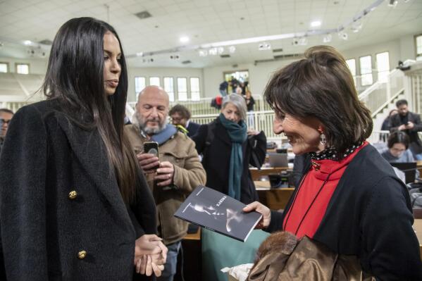 Karima El Mahroug, aka Ruby Rubacuori, one of the girls who attended the Bunga Bunga infamous parties, presents her book to prosecutor Tiziana Siciliano, right, at the trial's in the bunker room of Milan's San Vittore jail, Italy, Wednesday, Feb. 15, 2023. Verdict is expected for the 29 defendants in the Ruby Ter trial, among them former premier Silvio Berlusconi. He is accused of paying off witnesses for false testimony in earlier trials over his Bunga Bunga parties. (Claudio Furlan/LaPresse via AP)