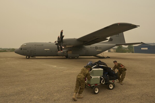 Royal Canadian Air Force Pte. Carter Brinn (left) and Cpl. Ethan Cai helps load cargo as evacuees from Pinaow Wachi Care Home board a C-130 Hercules aircraft in Norway House, Man., Tuesday, June 3, 2025, at the Norway House Airport as crews continue to fight wildfires in northern Manitoba. (David Lipnowski/The Canadian Press via AP)