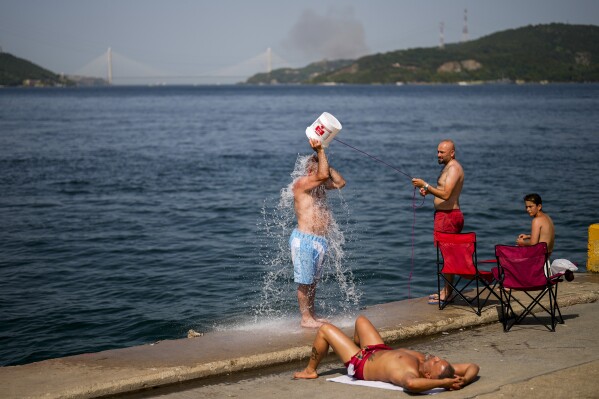 FILE - People cool off at the Bosphorus as forest fire smoke rises, background, during a hot summer day in Istanbul, Turkey, July 26, 2023. Scientists say by far the biggest cause of the recent extreme warming is human-caused climate change and a natural El Nino. But some say there’s got to be something more. (AP Photo/Francisco Seco, File)