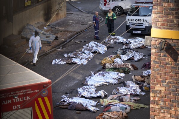 Medics stand by the covered bodies of victims of a deadly blaze in downtown Johannesburg, Thursday, Aug. 31, 2023. Dozens died when a fire ripped through a multi-story building in Johannesburg, South Africa's biggest city, emergency services said Thursday. (AP Photo/Jerome Delay)