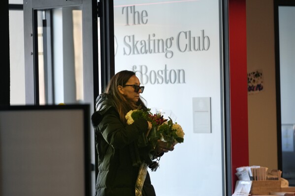 A woman brings flowers to The Skating Club of Boston, where six athletes, coaches and family associated with the club are believed to have perished in the collision of a passenger aircraft and military helicopter in Washington, Thursday, Jan. 30, 2025, in Norwood, Mass. (AP Photo/Robert F. Bukaty)