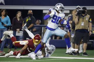 FILE - Dallas Cowboys defensive end DeMarcus Lawrence (90) breaks tackles on the way to the end zone for a touchdown after intercepting a pass throw by Washington Football Team's Taylor Heinicke (4) in the first half of an NFL football game in Arlington, Texas, Sunday, Dec. 26, 2021. The Cowboys are bringing back Lawrence on a new contract that will create more room under the salary cap, a person with knowledge of the agreement said Monday, March 14, 2022. (AP Photo/Ron Jenkins, File)