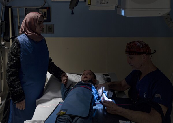 Orthopedic surgeon Dr. Scott Kozin, right, holds the arm of 4-year-old Omar Abu Kuwaik for an x-ray while Omar's aunt Maha Abu Kuwaik holds his hand at Shriners Children's Hospital, Thursday, Jan. 18, 2024, in Philadelphia. (AP Photo/Peter K. Afriyie)
