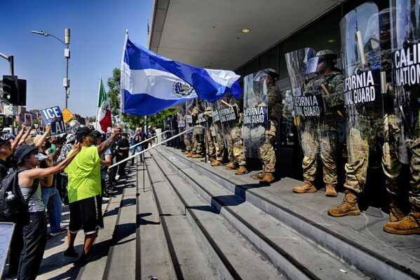 A protester waves a National Flag of El Salvador in front of a line of California National Guard in front of Federal Building on Monday, June 9, 2025, in downtown Los Angeles. (AP Photo/Eric Thayer)