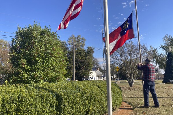 Lee Johnson, an employee of the town of Plains, Ga., lowers the American and Georgia state flags on the morning Monday, Nov. 20, 2023, to recognize the death of Rosalynn Carter. The former U.S. first lady died Sunday at the age of 96. She and former President Jimmy Carter were both born, married and lived most of their lives in their hometown of about 600 people. (AP Photo/Bill Barrow)