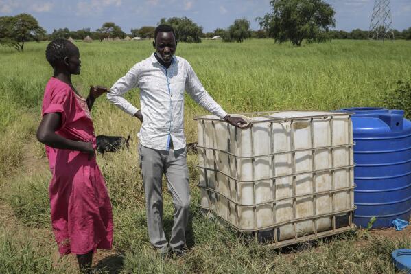 In this photo taken Monday, Oct. 1, 2018, residents stand next to a white container previously used for hazardous chemicals that was then used for several years to hold drinking water before the oil company put a stop to the practice, on the road between Melut and Paloch town, in South Sudan. The oil industry in South Sudan has left a landscape pocked with hundreds of open waste pits with the water and soil contaminated with toxic chemicals and heavy metals, and accounts of "alarming" birth defects, miscarriages and other health problems, according to four environmental reports obtained by The Associated Press. (AP Photo/Sam Mednick)