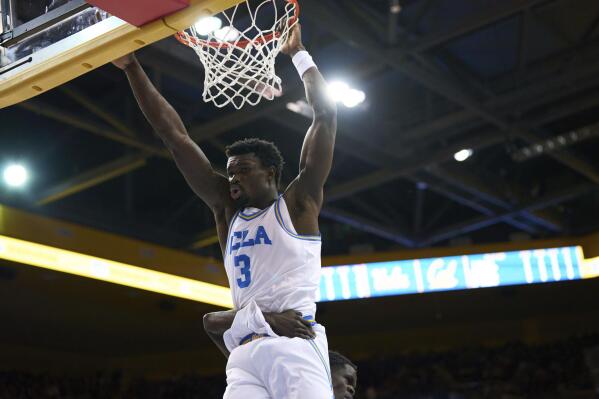 UCLA forward Adem Bona (3) hangs from the rim after a dunk, as a California player puts an arm around him during the first half of an NCAA college basketball game Saturday, Feb. 18, 2023, in Los Angeles. (AP Photo/Allison Dinner)
