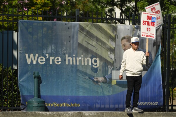 Boeing employee Som Dom, an electrician who has worked 17 years at Renton factory, holds a picket sign as workers strike Tuesday, Sept. 24, 2024, outside the company's factory in Renton, Wash. (AP Photo/Lindsey Wasson)