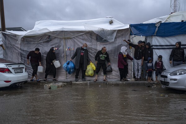 Palestinians displaced by the Israeli bombardment of the Gaza Strip seek cover from a winter rainfall at a U.N. tent camp in the southern town of Khan Younis, Gaza Strip, Sunday, Nov. 19, 2023. Hundreds of thousands of Palestinians have fled their homes in northern Gaza as Israel moves ahead with a ground offensive against the ruling Hamas militant group. (AP Photo/Fatima Shbair)