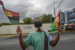 A man protests outside the British Council to demand an apology and slavery reparations during a visit to the former British colony by the Duke and Duchess of Cambridge, Prince William and Kate, in Kingston, Jamaica, Tuesday, March 22, 2022. The two-day visit to Jamaica is part of a larger trip to the Caribbean region encouraged by Queen Elizabeth II as some countries debate cutting ties with the monarchy like Barbados did late last year. (AP Photo/Collin Reid)