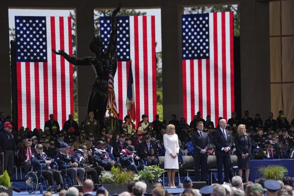 2024年6月6日，星期四，法国总统埃曼纽尔·马克隆（左二）、他的妻子布里吉特·马克隆（右二）、美国总统乔·拜登（右中）和第一夫人吉尔·拜登与二战退伍军人一起在诺曼底科利维尔附近的美国公墓参加仪式。来自美国、英国和加拿大的二战退伍军人本周将前往诺曼底，纪念导致希特勒失败的诺曼底登陆80周年。（美联社照片/Laurent Cipriani）