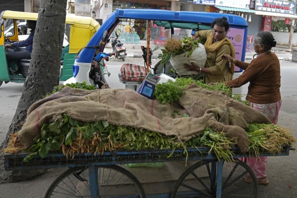 Preethi, left, a 38-year-old transgender woman who uses only her first name, hands over a sack of vegetables to her customer who traveled in her electric auto rickshaw in Bengaluru, India, Monday, July 10, 2023. (AP Photo/Aijaz Rahi)