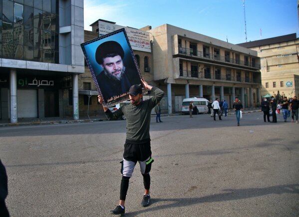 Followers of Shiite cleric Muqtada al-Sadr, in the poster, head to Tahrir Square, Baghdad, Iraq, Friday, Nov. 27, 2020. Thousands took to the streets in Baghdad on Friday in a show of support for a radical Iraqi cleric ahead of elections slated for next year, stirring fears of a spike in coronavirus cases. (AP Photo/Khalid Mohammed)