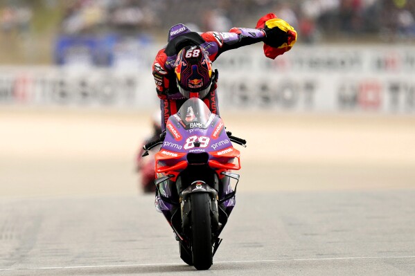 MotoGP rider Jorge Martin of Spain, holding a Spanish flag, bows as he returns to the pit lane after winning the MotoGP race of the Portuguese Motorcycle Grand Prix at the Algarve International circuit near Portimao, Portugal, Sunday, March 24, 2024. (AP Photo/Jose Breton)