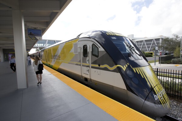 FILE -People walk near a Brightline train at a station, Jan. 11, 2018, in Fort Lauderdale, Fla. A proposed high-speed passenger train between Las Vegas and Southern California got another boost on Tuesday, Jan. 23, 2024, with Biden administration approval to issue another $2.5 billion in tax-exempt bonds for the $12 billion project. (AP Photo/Wilfredo Lee, File)