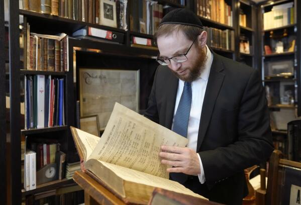 Rabbi Nicky Liss looks through items in a collection belonging to Professor David Latchman of memorabilia related to the history of British Jews, in London, Friday, April 28, 2023. Rabbi Nicky Liss won’t be watching King Charles III’s coronation. He’ll be doing something more important praying for the monarch on the Jewish sabbath. On Saturday, he will join rabbis across Britain in reading a prayer in English and Hebrew that gives thanks for the new king in the name of the “one God who created us all.” (AP Photo/Kirsty Wigglesworth)