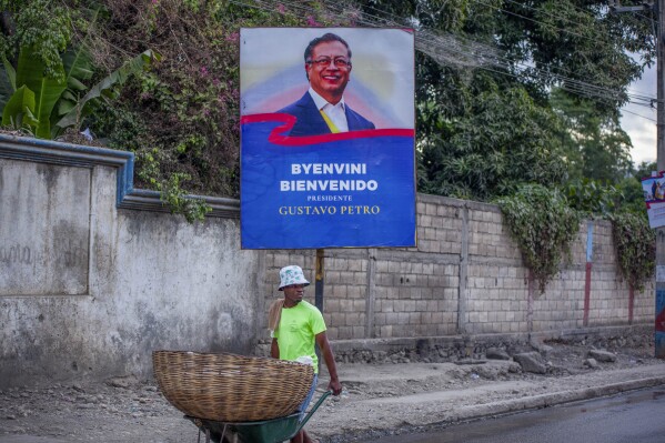 A street vendor walks past a poster welcoming Colombian President Gustavo Petro for a one-day visit, in Jacmel, Haiti, Wednesday, Jan. 22, 2025. (AP Photo/Patrice Noel)