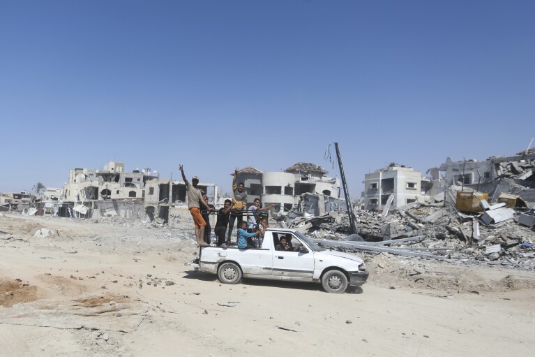 Los palestinos pasan junto a la devastación causada por el ataque aéreo y terrestre israelí después de su retirada de Khan Yunis, en el sur de la Franja de Gaza, el domingo 7 de abril de 2024. (Foto AP/Ismael Abu Dayyah)