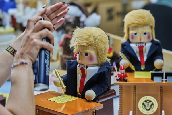 An employee sprays the hair on a limited-edition nutcracker titled “Resolute Desk of the President,” featuring a seated Trump-like figure signing a “presidential proclamation,” at the Steinbach-Volkskunst nutcracker factory in Marienberg, Germany, April 15, 2025. (AP Photo/Markus Schreiber)