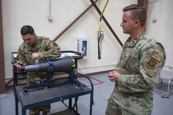 In this image provided by the U.S. Air Force, Staff Sgt. Brandon Mendola, left, with the 90th munitions squadron at F.E. Warren Air Force Base in Wyoming demonstrates how they train new missile maintainers to look for scratches on the top of a nuclear warhead. Even a hairline scratch on the polished black surface of the cone could create enough drag when fired to send the weapon off course, so maintainers inspect the devices closely. (Senior Airman Sarah Post/U.S. Air Force via AP)