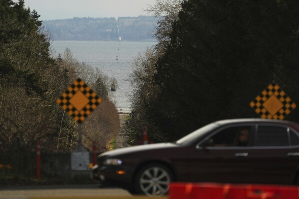 Towers in the water denote the international boundary line between Canada, at left, and the United States, at right, as a car approaches the border checkpoint heading into Canada, Tuesday, March 18, 2025, in Point Roberts, Wash. (AP Photo/Lindsey Wasson)