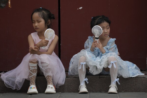 ARCHIVO - Los niños se refrescan con ventiladores eléctricos mientras descansan cerca de la Ciudad Prohibida en un día caluroso en Beijing, el 25 de junio de 2023. La Administración Nacional Oceánica y Atmosférica dijo el jueves 13 de julio que una Tierra que ya se estaba calentando llegó a su junio más caluroso. en expediente. (Foto AP/Andy Wong, archivo)