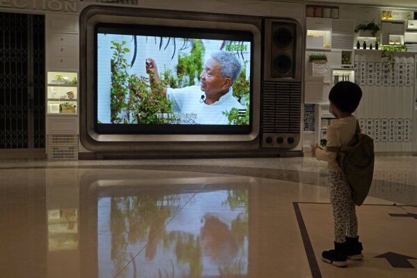 A TV screen shows a footage of Arthur Lee, owner of the MoVertical Farm, at a supermarket in Hong Kong Thursday, Sept. 24, 2020. Operating on a rented 1,000 square meter patch of wasteland in Hong Kong's rural Yuen Long, Arthur Lee's MoVertical Farm utilizes around 30 of the decommissioned containers, to raise red water cress and other local vegetables hydroponically, which eliminates the need for soil. A few are also used as ponds for freshwater fish, with the bounty sold to local supermarkets in this crowded city of 7.5 million that is forced to import most of its food. (AP Photo/Kin Cheung)
