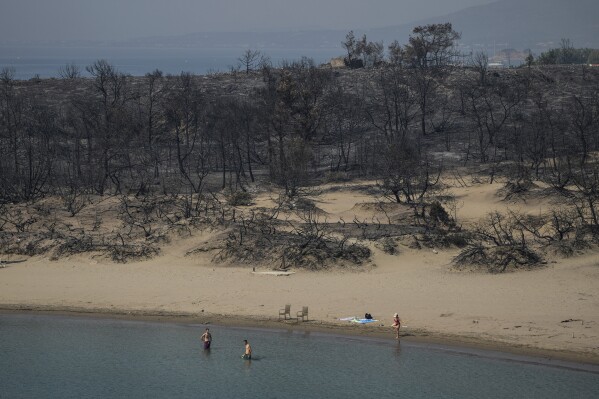 People gather on a beach in front of forest burnt in wildfires near Gennadi village, on the Aegean Sea island of Rhodes, southeastern Greece, on  July 27, 2023. (AP Photo/Petros Giannakouris)