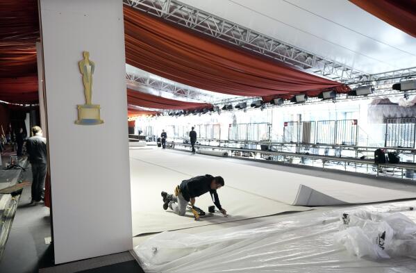 REMOVES REFERENCE TO CARPET COLOR - A crew member staples the carpet to the ground in preparation for Sunday's 95th Academy Awards, Wednesday, March 8, 2023, outside the Dolby Theatre in Los Angeles. (AP Photo/Chris Pizzello)