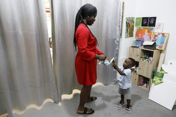 Chantelle Kukwa Egan, de 25 años, le da pintura a su hijo Ace Liam Nana Sam Ankrah, que cumplirá 2 años en julio, en la galería de arte de su madre en Accra, Ghana, el lunes 27 de mayo de 2024. El artista masculino más joven.  Egan dice que todo empezó por casualidad cuando su hijo, que en ese momento tenía 6 meses, descubrió sus pinturas.  (Foto AP/Misper Apawu)