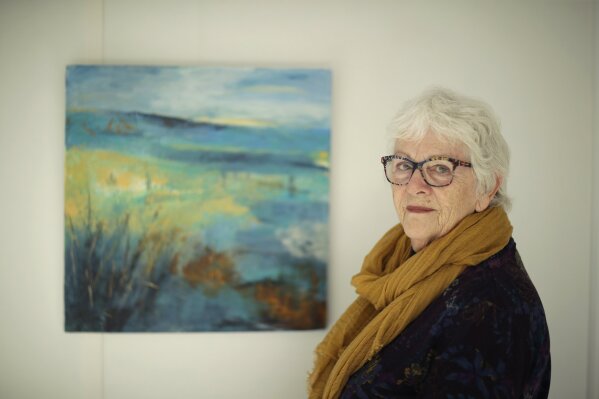 FILE - In this Wednesday, April 10, 2019 file photo, Elly Wright, a Dutch painter who has lived in Britain for 51-years, poses for photographs next to one of her own paintings at her home in Epsom, on the south west edge of London. Anxious, angry, abandoned. Brexit elicits strong emotions, and as Britain’s departure from the European Union approaches, more than 3 million U.K. residents who are citizens of EU countries feel the impending separation more strongly than most. (AP Photo/Matt Dunham, File)
