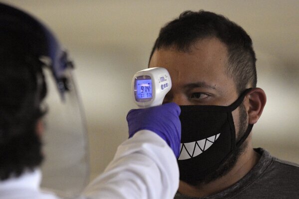 Jose Ramirez has his temperature checked before entering Universal CityWalk, Thursday, June 11, 2020, near Universal City, Calif. The tourist attraction, which had been closed due to the coronavirus outbreak recently re-opened. The Universal Studios tour is still closed. (AP Photo/Mark J. Terrill)