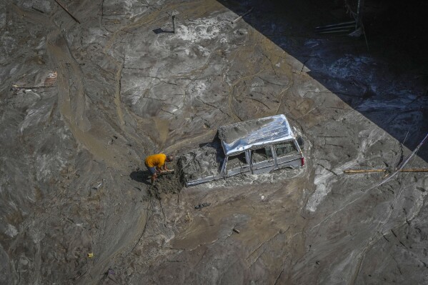 A man tries to recover a vehicle submerged in mud in the flood-affected area along the Teesta river in Rongpo, east Sikkim, India, Sunday, Oct. 8. 2023. (AP Photo/Anupam Nath)