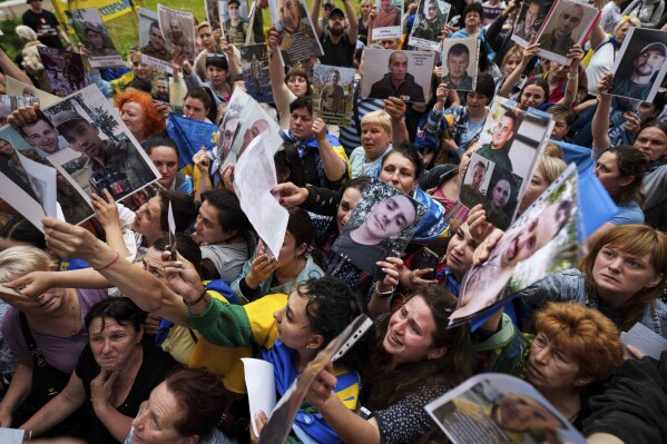 People show photos of their missed relatives to Ukrainian soldiers during a POWs exchange between Russia and Ukraine, in Chernyhiv region, Ukraine, Saturday, May 24, 2025. (AP Photo/Evgeniy Maloletka)