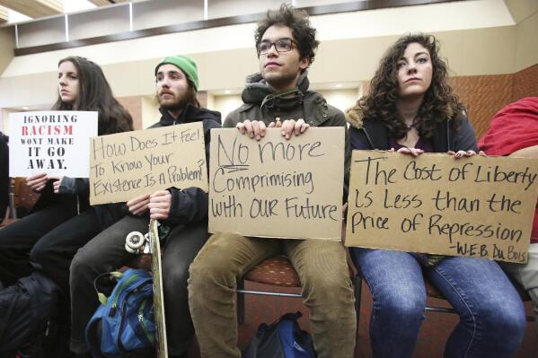 FILE - University of Wisconsin-Madison students, from left, Marisa Skelley, Martin Jarzyna, Sam Broadnax and Morgan Menke hold up signs protesting racism on campus during a meeting for the UW System Board of Regents on campus in Madison, Wis., Dec. 11, 2015. The debate over free speech and racial equity on Wisconsin's college campuses is intensifying. In a span of days after a student posted racial slurs, a top Republican proposed eliminating campus diversity offices and a medical college cancelled a diversity symposium. (Amber Arnold/Wisconsin State Journal via AP, File)