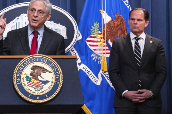 FILE - DEA Principal Deputy Administrator Louis Milione, right, stands behind Attorney General Merrick Garland during the announcement of an international law enforcement operation targeting fentanyl and opioid traffickers on the Darknet during a news conference at the Department of Justice, Tuesday, May 2, 2023, in Washington. In September 2023, Milione, the U.S. Drug Enforcement Administration’s recently departed second-in-command returned for a new stint with Guidepost Solutions, the high-powered consulting firm where he previously advised Purdue Pharma and a drug distributor fighting sanctions over a deluge of suspicious painkiller shipments. (AP Photo/Nathan Howard, File)