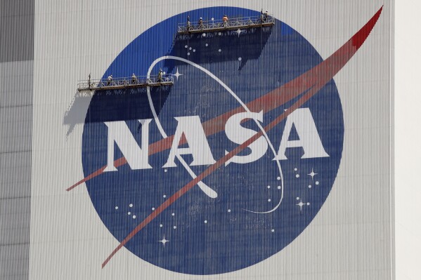 FILE - Workers on scaffolding repaint the NASA logo near the top of the Vehicle Assembly Building at the Kennedy Space Center in Cape Canaveral, Fla., Wednesday, May 20, 2020. After a yearlong study into UFOs, NASA is releasing a report Thursday, Sept. 14, 2023, on what it needs to better understand unidentified flying objects from a scientific point of view. (AP Photo/John Raoux, File)