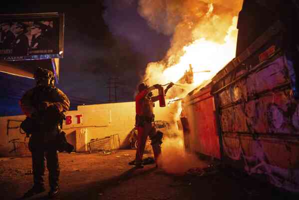 A law enforcement officer works to put out a fire during a protest in Compton, Calif., Saturday, June 7, 2025, after federal immigration authorities conducted operations. (AP Photo/Ethan Swope)