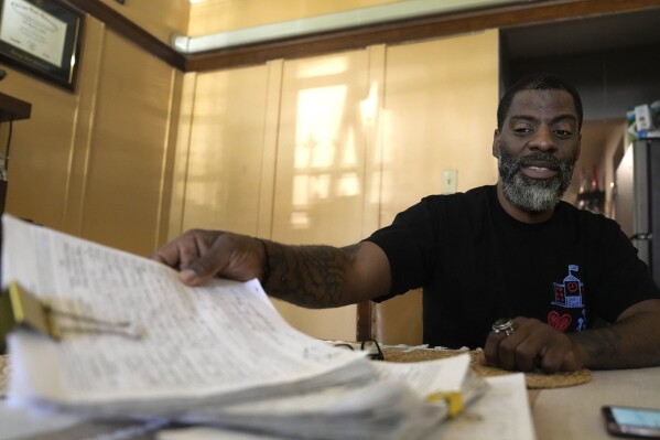 Chicago School Board candidate, rapper Che "Rhymefest" Smith, looks over signature petitions for his candidacy during an interview with The Associated Press at his home in the Chatham neighborhood of Chicago, Tuesday, May 21, 2024. The nation's third-largest city is preparing for its first-ever school board elections and the slate of potential candidates include progressive activists, an afterschool squash program leader and a Grammy-winning rapper. (AP Photo/Charles Rex Arbogast)